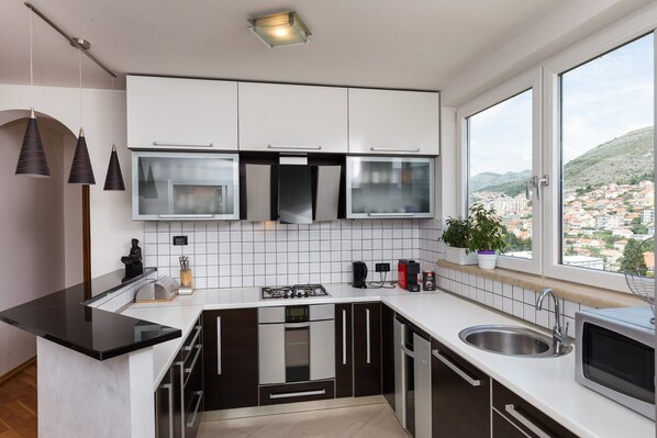 A modern kitchen with white cabinets, stainless steel appliances, a black countertop, and a window with a city view.