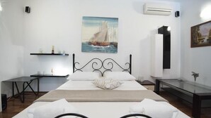 Habitación de hotel con una cama grande, un cuadro de un velero en la pared, una mesita y un banco.