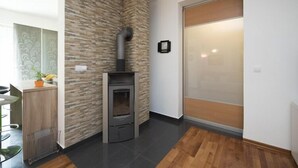 Una cocina moderna con un horno a leña empotrado, un comedor con una mesa y sillas de madera, y un ventanal corredero que da a un balcón.