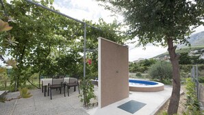 Un patio exterior con una mesa y sillas, una piscina pequeña y una pérgola que ofrece sombra.