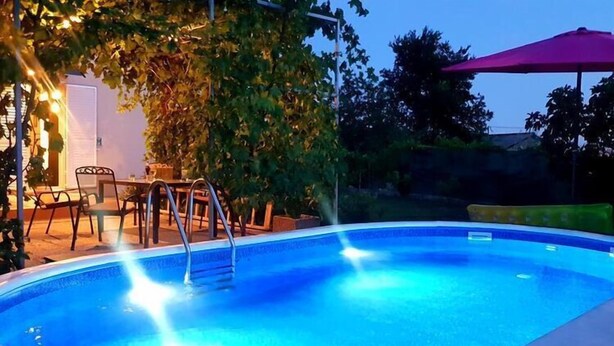 Una piscina con escalera, rodeada de mobiliario exterior y una pérgola.
