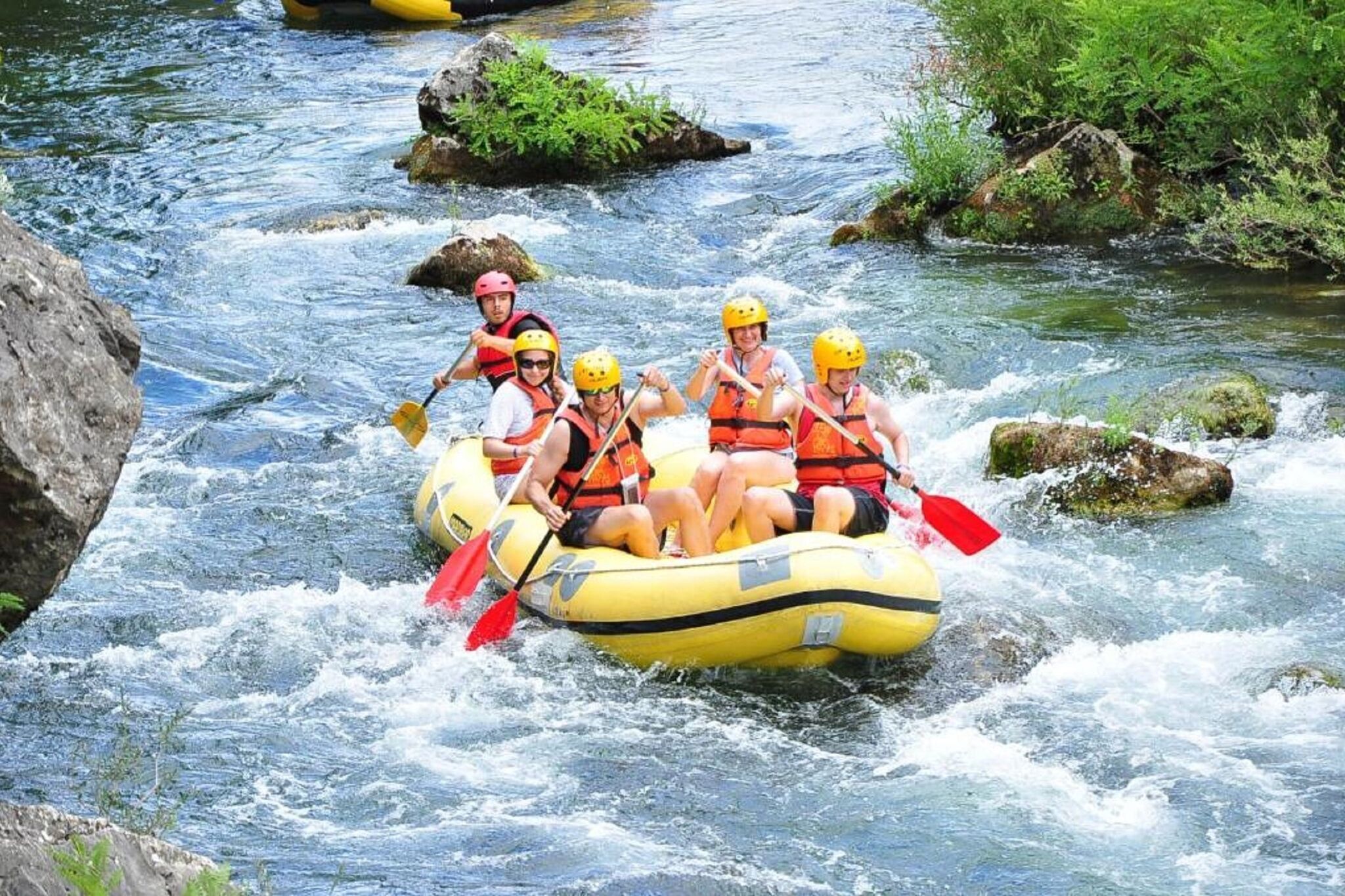 A group of people in a yellow raft navigating a river with rapids.