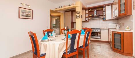 A dining area with a round table set for four, wooden chairs, and a kitchen with cabinets and appliances.