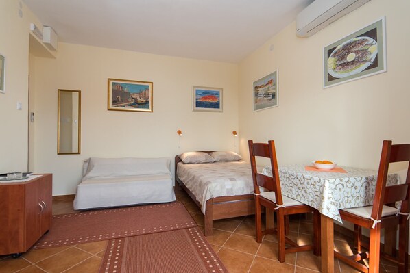 A bedroom with a single bed, a bedside table, and a small desk with a chair. There are two framed pictures on the wall, a window, and a tiled floor. - Pulastar - Studio Apartment with Terrace (Dubrovnik)