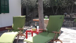 Zwei grüne Loungesessel mit Holzgestellen, ein kleiner roter Tisch mit einer Flasche und einer Schale, und eine Steinmauer im Hintergrund.
