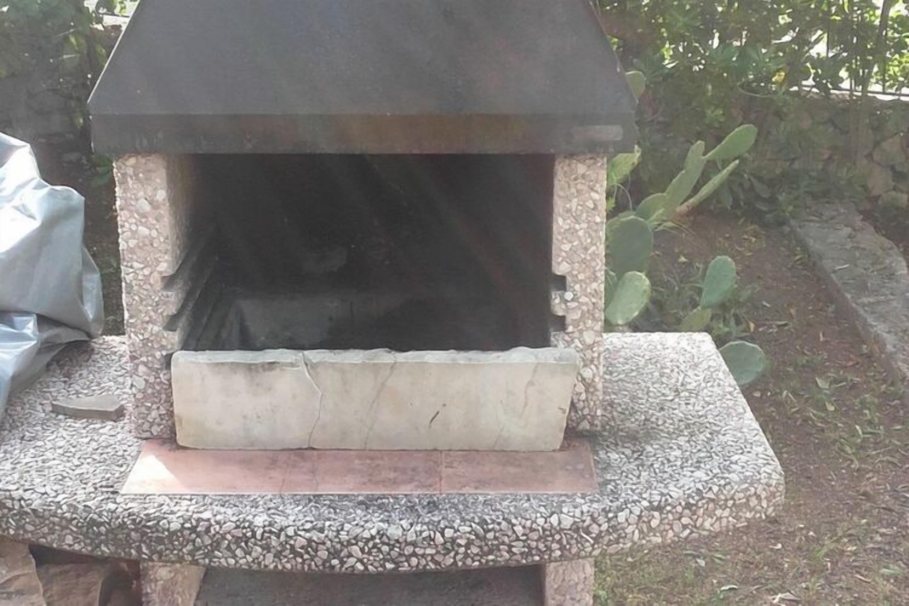 A stone-built outdoor oven with a black roof, surrounded by gravel and plants.