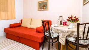 Una sala de estar acogedora con un sofá rojo, una mesita redonda con mantel blanco y dos sillas.