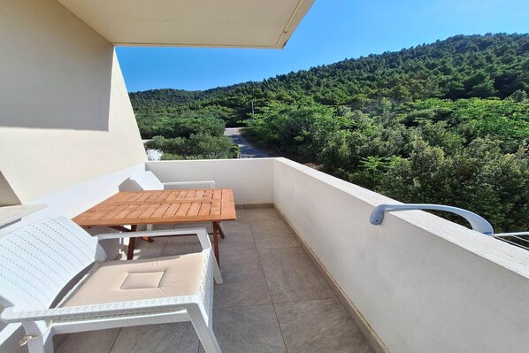 Un balcon avec une chaise blanche, une table en bois et une vue sur une colline boisée.