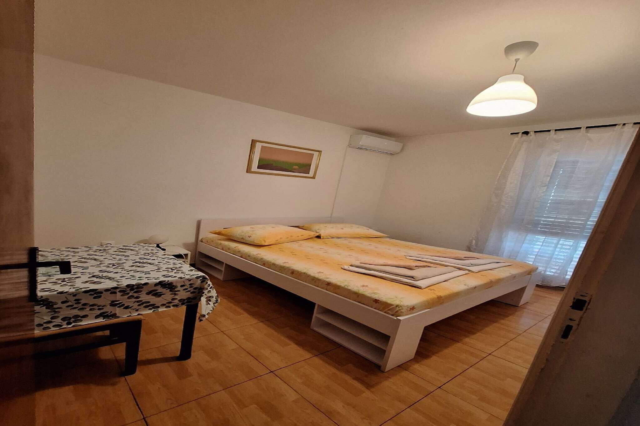 Una habitación pequeña y limpia con cama, una mesa y ventilador de techo.