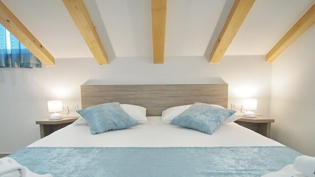Une chambre d’hôtel avec un grand lit, deux tables de chevet avec des lampes et un plafond en bois.