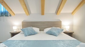 Habitación de hotel con una cama grande, vigas de madera en el techo, dos lámparas de noche y una colcha azul.