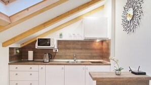 Una cocina moderna con techo de madera, armarios blancos, un microondas, un lavamanos y un elemento decorativo en la pared.