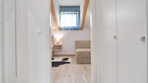 Una habitación con techo inclinado, una ventana con cortinas azules, una mesita de noche con lámpara, un sofá y un tapete de cuero de vaca.