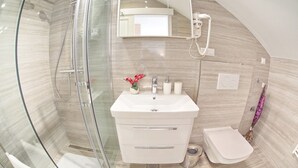 Et moderne badeværelse med en brusekabine i glas, en hvid vask med et spejl over, og et toilet.