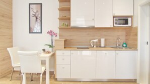 Et moderne køkken med lyse skabe, en mikrobølgeovn og en vask. Der er et spisebord med stole og en vase med blomster.