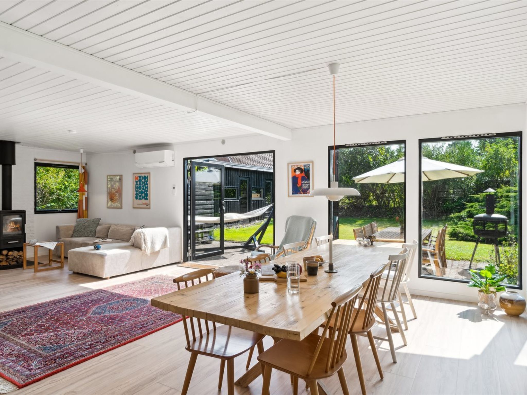 Un vaste espace de vie comprenant une table à manger en bois, des sièges confortables, une grande fenêtre donnant sur le jardin et une cheminée intégrée.