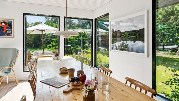 A modern dining area with a wooden table, chairs, and a view of a lush garden through large windows.