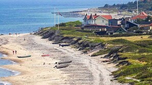 A beach with boats, a sandy shore, and houses with red roofs.