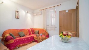 Een gezellige woonkamer met een bank, een eettafel met een schaal fruit, en een houten deur.