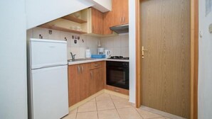 Een kleine keuken met witte kastjes, een witte koelkast, een fornuis en een houten deur.