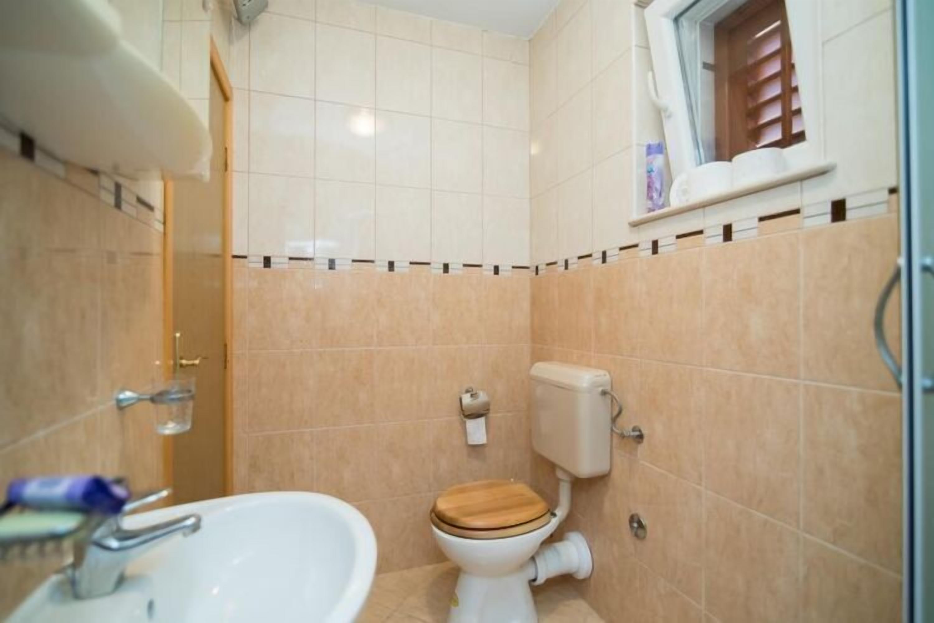 A small bathroom with a toilet, sink, and a window with blinds.
