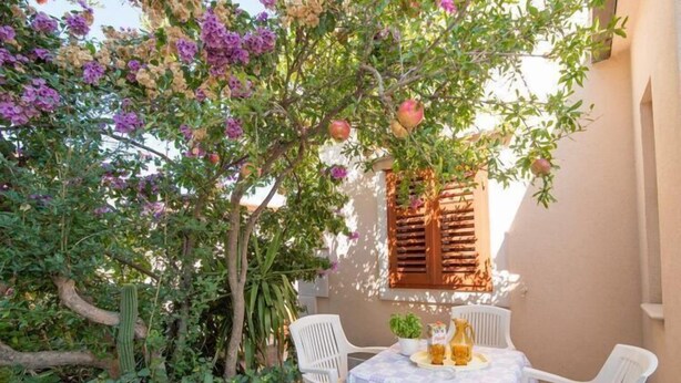 Eine Terrassengruppe im Freien mit Tisch für zwei Personen, umgeben von üppigem Grün und blühenden Pflanzen.
