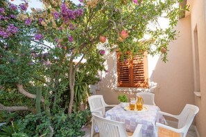 Une terrasse extérieure avec une table dressée pour deux personnes, entourée d’une végétation luxuriante et de plantes en fleurs.