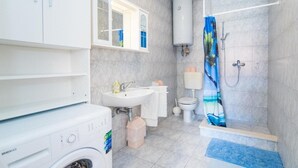 A bathroom with a washing machine, a sink, a toilet, and a shower with a curtain.
