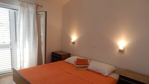 A bedroom with a bed, two bedside tables, a nightstand, and a window with curtains.