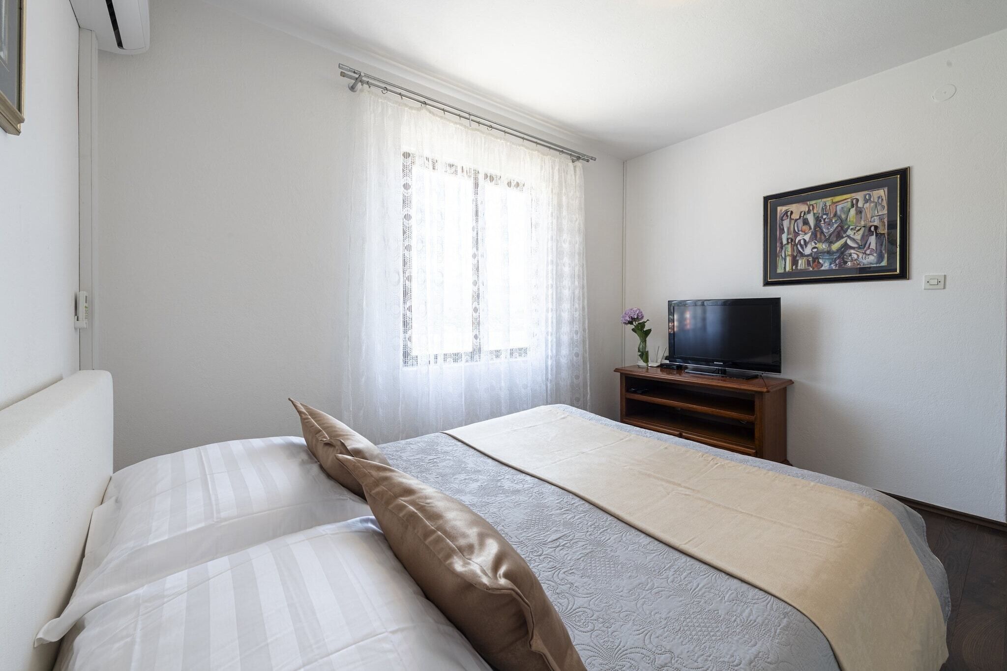 Habitació d'hotel amb un llit, una televisió sobre un suport de fusta i un quadre a la paret.