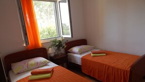 Een kamer met twee bedden, elk met een oranje sprei en een kussen met een rond patroon. Er staat een nachtkastje met een lamp en een vaas met bloemen tussen de bedden.