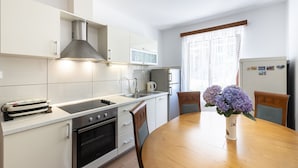 A modern kitchen with white cabinets, a stainless steel range hood, a microwave, and a refrigerator. There is a dining table with chairs and a vase of flowers. - Guest House Rooms Rose- Comfort Double Room with Balcony and Sea View (Molunat)