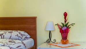 En pænt redt seng med blomstret sengetøj, en sengetøjslampe og en vase med blomster på et lille bord ved siden af sengen.