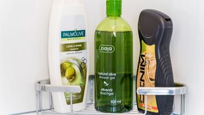 En hylde med tre flasker flydende produkter, heriblandt shampoo, badesæbe og en hårtørrer.