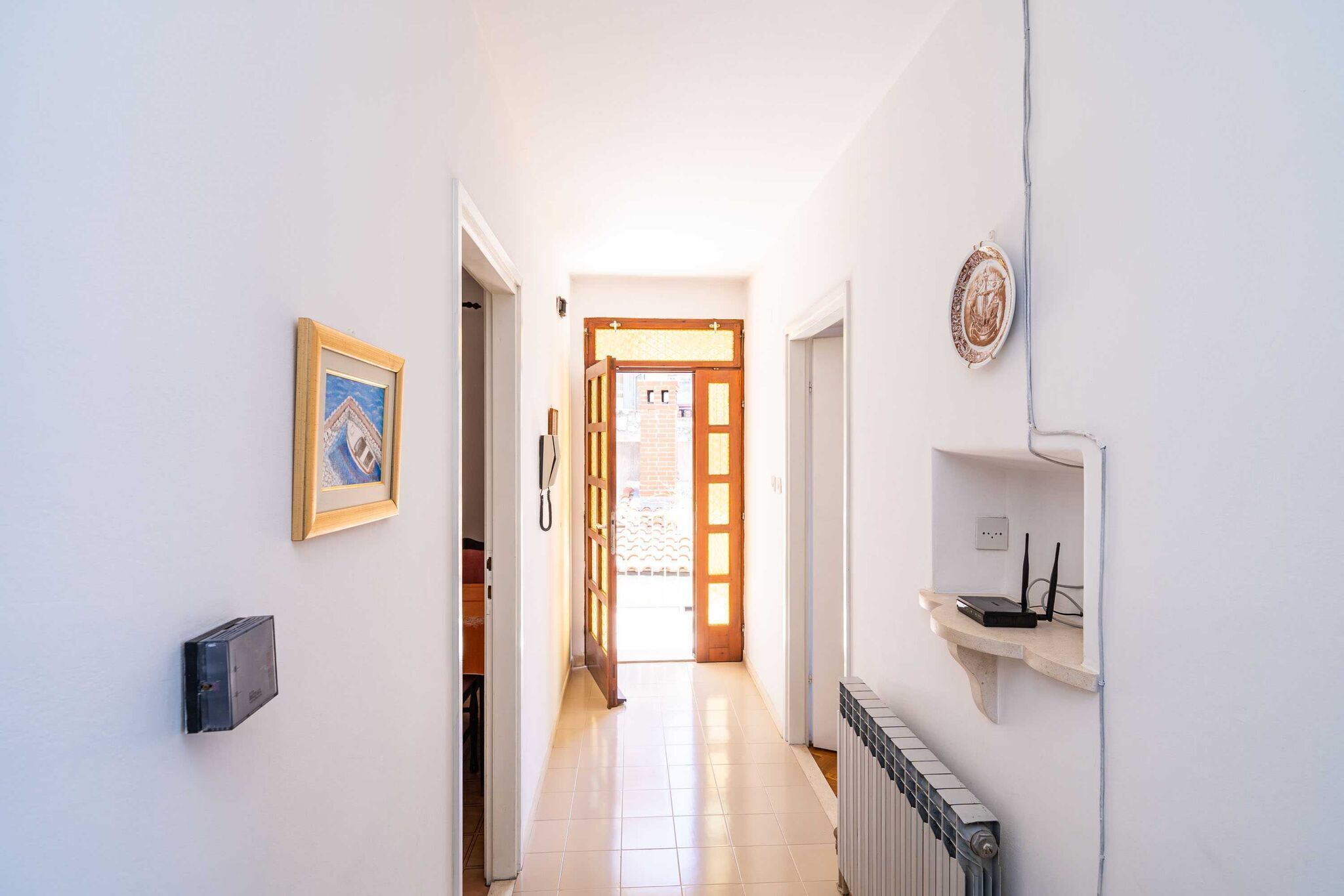A hallway with a door leading to an outdoor area, a framed picture on the wall, and a shelf with electronic devices.