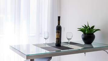 Una mesa de vidrio con una botella y dos copas, una planta en maceta y una ventana con cortinas.