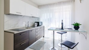 A modern kitchen with a marble backsplash, dark cabinets, and a glass dining table with two bar stools. - Apartment Lea - Studio Apartment (Dubrovnik)