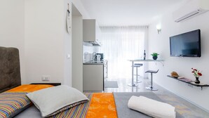 A compact hotel room with a bed, a small kitchenette, a TV, and a view of the kitchen. - Apartment Lea - Studio Apartment (Dubrovnik)