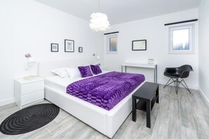 Une chambre moderne avec un lit blanc, une literie violette, un bureau noir et une chaise noire.