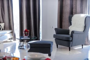 A modern living room with a grey armchair, a glass coffee table, and a dining area with a white table and chairs.