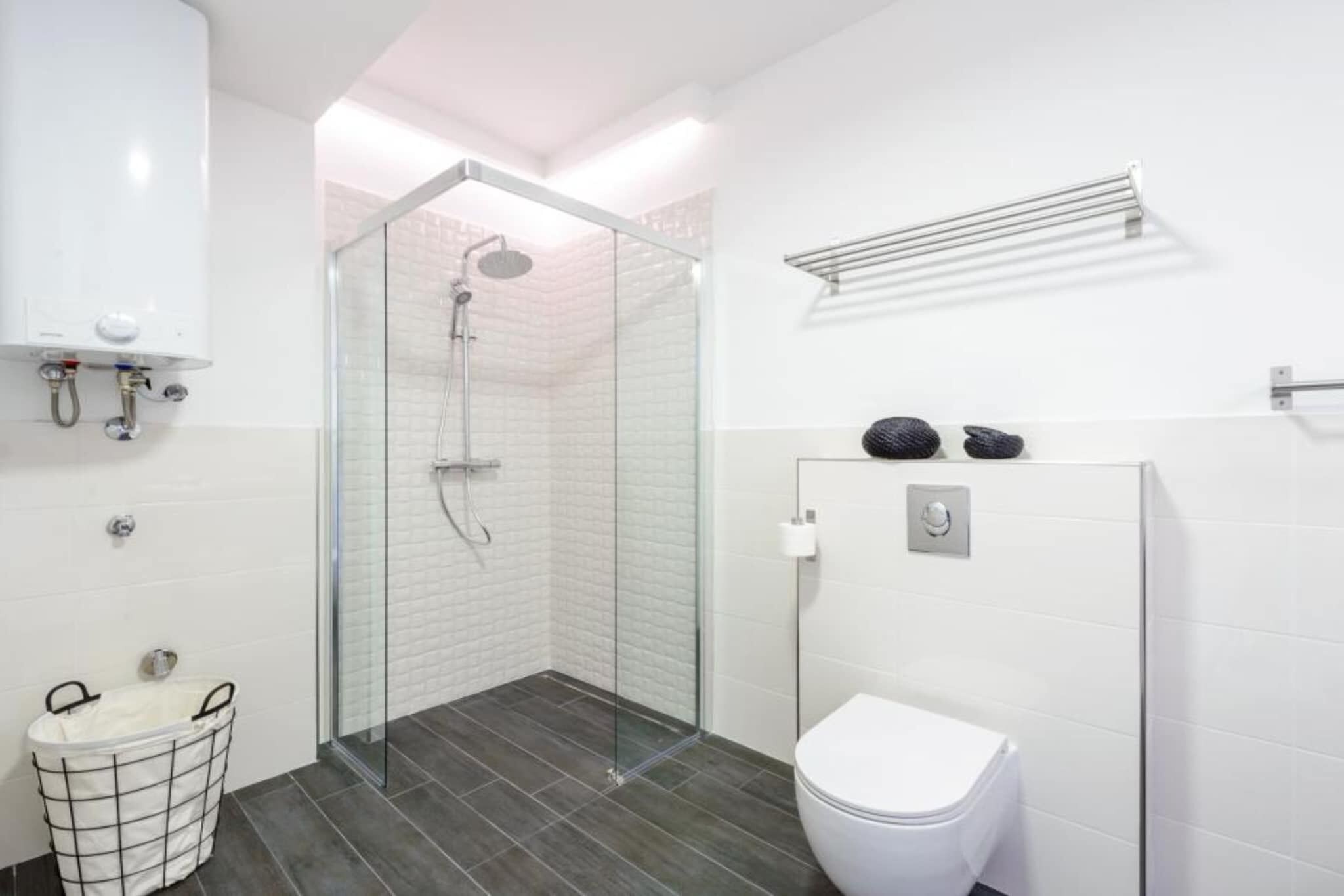 A modern bathroom with a glass-enclosed shower, a white toilet, and a metal towel rack.