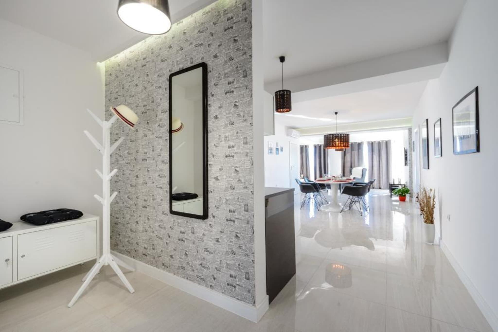 Ein modernes Interieur mit einem weißen Schrank, einem großen Spiegel und einem Essbereich mit einer Chandelüster.