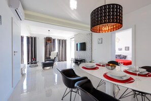 Un espace repas moderne avec une table blanche, des chaises noires et un grand luminaire suspendu.