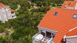 A residential building with a red-tiled roof, a balcony with a glass railing, and a view of a green landscape and a body of water.