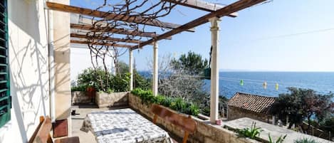 A covered outdoor seating area with a table and benches, overlooking a coastal view.