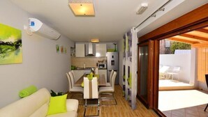 Un espai habitable compacte amb zona de menjador, petita cuina i una porta corredissa de vidre que dona a un pati exterior.