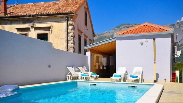 Una piscina amb gandules, un edifici amb teulada ceràmica i un paisatge de muntanyes al fons.