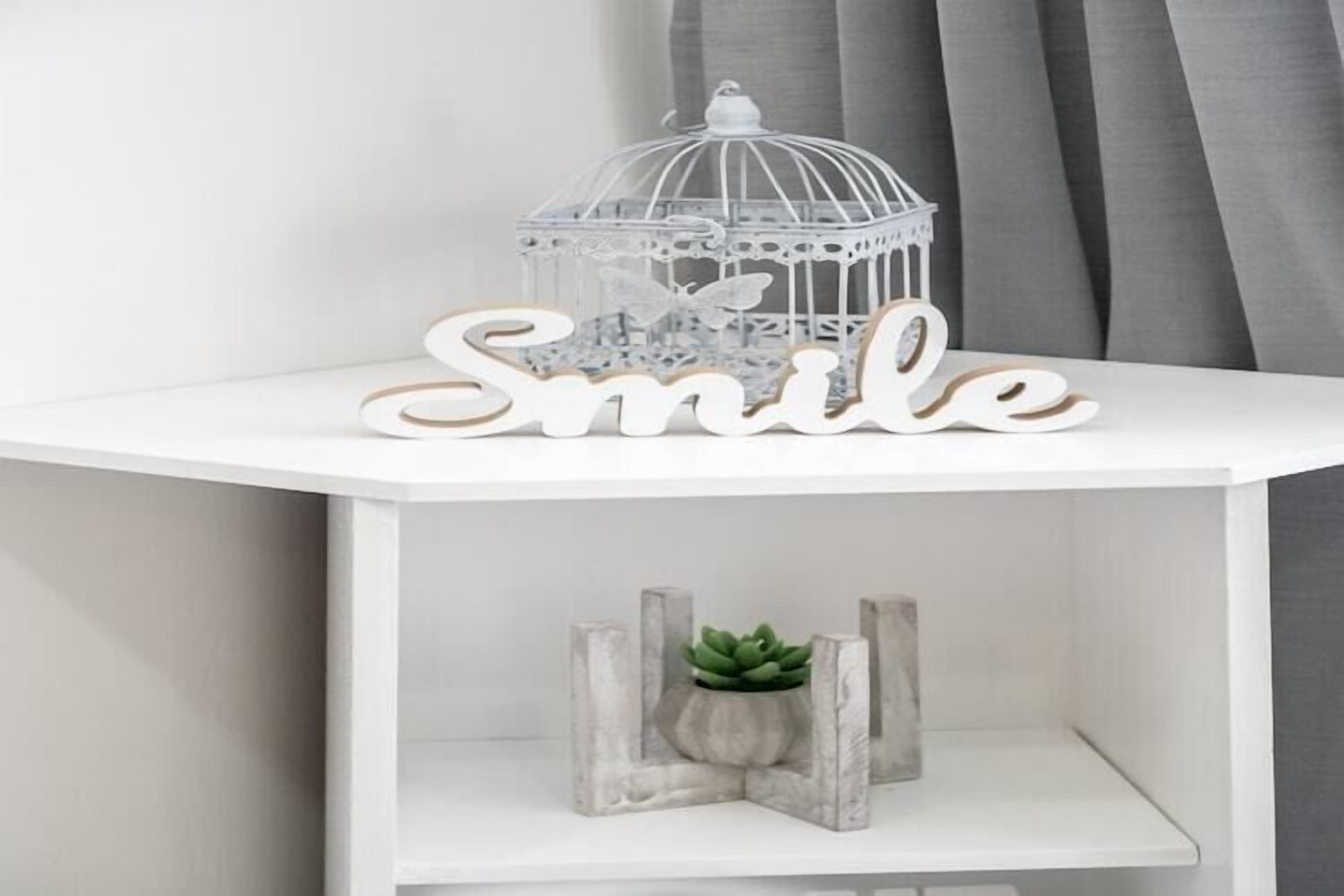 A white shelf with a 'Smile' sign, a white birdcage, and a small potted plant.
