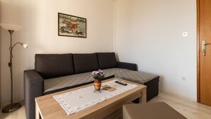 A living room with a sofa, a coffee table with a vase and remote control, and a painting on the wall. - Apartments Belenum - One-Bedroom Apartment with Balcony and Sea View (no.3) (Mlini)