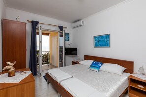 Ett hotellrum med en säng, ett nattduksbord, en tv och utsikt genom en glasdörr ut mot ett utomhusområde.